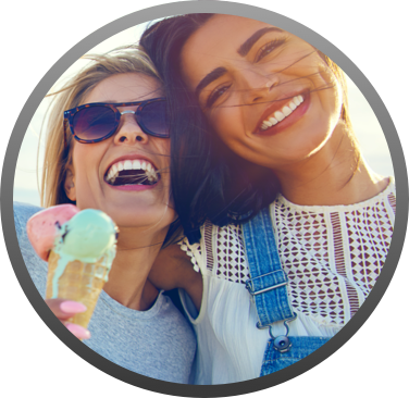 Two ladies smiling, one of whom is holding a double scoop ice cream cone